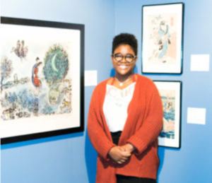 A Student poses with framed art in a gallery